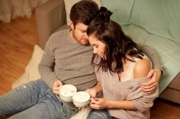 hygge, leisure and people concept - happy couple drinking cacao with marshmallow and hugging at home. happy couple drinking cacao at home. happy couple drinking cacao at home