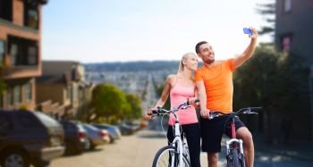 fitness, sport, technology and healthy lifestyle concept - happy couple riding bicycles and taking selfie by smartphone over san francisco city background. couple with bicycles taking selfie by smartphone. couple with bicycles taking selfie by smartphone