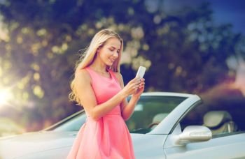 road trip, technology and communication concept - happy young woman with smartphone at convertible car over summer background. young woman with smartphone at convertible car. young woman with smartphone at convertible car