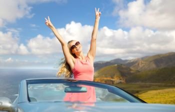 travel, summer holidays, road trip and people concept - happy young woman wearing sunglasses in convertible car showing peace sign over bixby creek bridge on big sur coast of california background. happy woman in convertible car on big sur coast. happy woman in convertible car on big sur coast