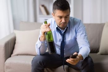 alcoholism, alcohol addiction and people concept - drunk man with smartphone and bottle of wine at home. man with smartphone and bottle of alcohol at home. man with smartphone and bottle of alcohol at home