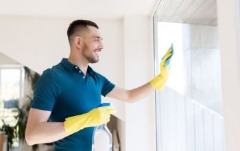 household and people concept - man in rubber gloves cleaning window with rag and spray cleaner at home. man in rubber gloves cleaning window with rag. man in rubber gloves cleaning window with rag
