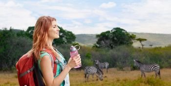 adventure, travel, tourism, hike and people concept - smiling young woman with backpack and bottle of water over zebras in african savannah background. happy woman with backpack over african savannah. happy woman with backpack over african savannah