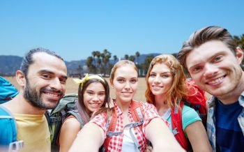 technology, travel, tourism, hike and people concept - group of smiling friends with backpacks taking selfie over venice beach background in california. friends with backpack taking selfie over beach. friends with backpack taking selfie over beach