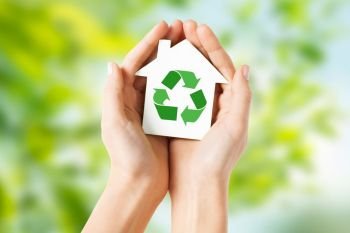 ecology, environment and conservation concept - close up of hands holding house with green recycling sign over natural background. hands holding house with green recycling sign. hands holding house with green recycling sign