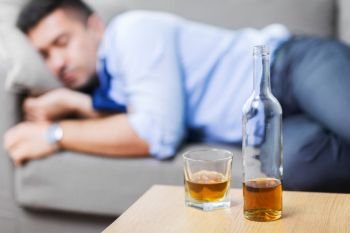 alcoholism, alcohol addiction and people concept - bottle with glass of whiskey on table and sleeping drunk man. bottle of alcohol on table and sleeping drunk man. bottle of alcohol on table and sleeping drunk man