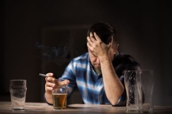 alcoholism, alcohol addiction and people concept - male alcoholic drinking beer and smoking cigarette at night. drunk man drinking alcohol and smoking cigarette. drunk man drinking alcohol and smoking cigarette