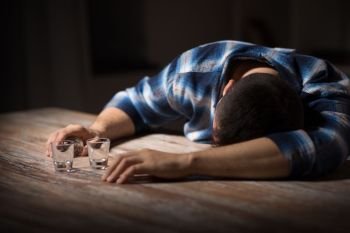 alcoholism, alcohol addiction and people concept - male alcoholic with empty glasses lying or sleeping on table at night. drunk man with empty glasses on table at night. drunk man with empty glasses on table at night