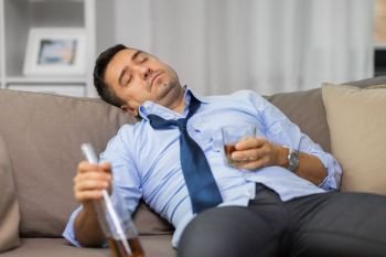 alcoholism, alcohol addiction and people concept - drunk man or alcoholic sleeping with bottle of whiskey on sofa at home. drunk man with bottle of alcohol sleeping at home. drunk man with bottle of alcohol sleeping at home