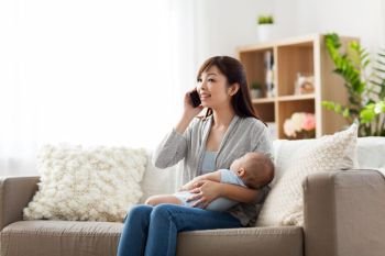 family, technology and motherhood concept - happy smiling young asian mother with sleeping baby calling on smartphone at home. mother with baby calling on smartphone at home. mother with baby calling on smartphone at home