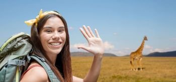 adventure, travel, tourism, hike and people concept - smiling young woman with backpack over giraffe in african savannah background. happy woman with backpack over savannah. happy woman with backpack over savannah