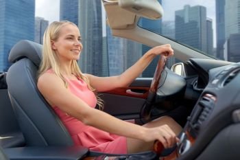 travel, road trip and people concept - happy young woman driving convertible car over singapore city skyscrapers background. woman driving convertible car over singapore city. woman driving convertible car over singapore city