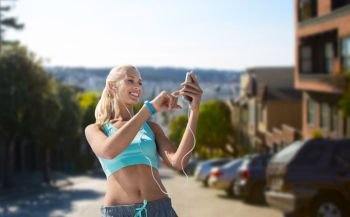 sport, technology and healthy lifestyle concept - smiling young woman with smartphone, earphones and fitness tracker listening to music and exercising over san francisco city background. woman with smartphone and earphones doing sports. woman with smartphone and earphones doing sports