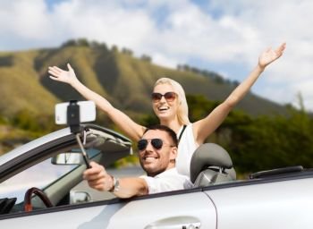 road trip, technology and travel concept - happy couple driving in convertible car and taking picture by smartphone on selfie stick. happy couple in car taking selfie by smartphone. happy couple in car taking selfie by smartphone