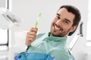medicine, dentistry and healthcare concept - happy smiling male patient with toothbrush on chair at dental clinic. smiling man with toothbrush at dental clinic. smiling man with toothbrush at dental clinic