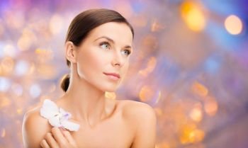 wellness and beauty concept - beautiful bare woman with orchid flower over holidays lights background. woman with orchid flower over green background. woman with orchid flower over green background