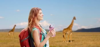 adventure, travel, tourism, hike and people concept - smiling young woman with backpack and bottle of water over giraffe in african savannah background. happy woman with backpack over african savannah. happy woman with backpack over african savannah