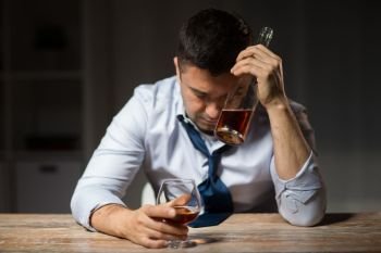 alcoholism, alcohol addiction and people concept - male alcoholic with bottle drinking brandy at table at night. drunk man drinking alcohol at table at night. drunk man drinking alcohol at table at night