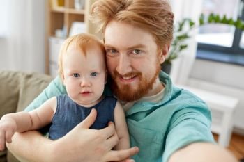 family, fatherhood and people concept - happy red haired father with little baby daughter taking selfie at home. happy father with baby taking selfie at home. happy father with baby taking selfie at home