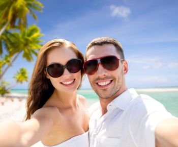 travel, tourism and summer vacation concept - smiling couple wearing sunglasses making selfie over tropical beach background in french polynesia. couple in sunglasses making selfie over beach. couple in sunglasses making selfie over beach