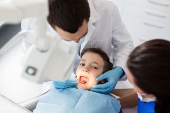 medicine, dentistry and healthcare concept - dentist with mouth mirror checking for kid patient teeth at dental clinic. dentist checking for kid teeth at dental clinic. dentist checking for kid teeth at dental clinic