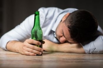 alcoholism, alcohol addiction and people concept - male alcoholic with beer bottle lying or sleeping on table at night. drunk man with beer bottle lying on table at night. drunk man with beer bottle lying on table at night
