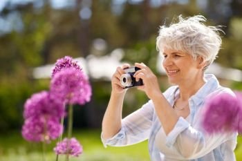 photography, leisure and people concept - happy senior woman with camera photographing flowers blooming at summer garden. senior woman with camera photographing flowers. senior woman with camera photographing flowers
