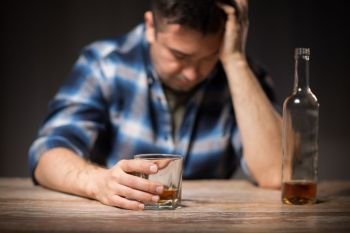 alcoholism, alcohol addiction and people concept - male alcoholic with bottle and glass drinking whiskey at night. alcoholic with glass drinking whiskey at night. alcoholic with glass drinking whiskey at night