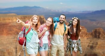 travel, tourism, hike and adventure concept - group of smiling friends with backpacks pointing finger to something over grand canyon national park background. group of friends with backpacks at grand canyon. group of friends with backpacks at grand canyon