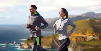 fitness, sport, people and healthy lifestyle concept - happy couple running over bixby creek bridge on big sur coast of california background. happy couple running outdoors. happy couple running outdoors