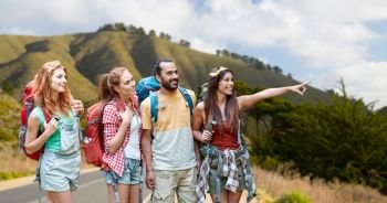 adventure, travel, tourism, hike and people concept - group of smiling friends with backpacks pointing finger over big sur coast of california hills background. group of friends with backpacks on big sur hills. group of friends with backpacks on big sur hills