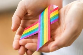homosexual and lgbt concept - close up of female hands holding gay pride awareness ribbon. female hands holding gay pride awareness ribbon. female hands holding gay pride awareness ribbon