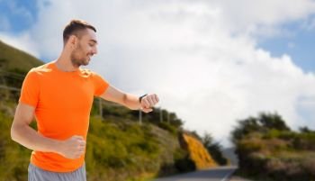sport, technology and healthy lifestyle concept - smiling young man with smart watch or fitness tracker over big sur hills and road background in california. man with smart watch or fitness tracker. man with smart watch or fitness tracker