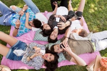 friendship, leisure, technology and people concept - group of friends with smartphones chilling on picnic blanket at summer park. friends with smartphones on picnic blanket. friends with smartphones on picnic blanket