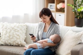 family, technology and motherhood concept - happy young asian mother with sleeping baby and smartphone at home. mother with sleeping baby and smartphone at home. mother with sleeping baby and smartphone at home