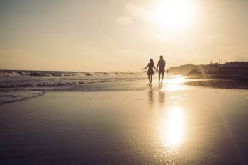 Silhouette of loving couple that walking along a sandy beach and enjoying sunset. Young romantic couple at the coastline