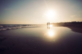 Silhouette of loving couple that walking along a sandy beach and enjoying sunset. Young romantic couple at the coastline