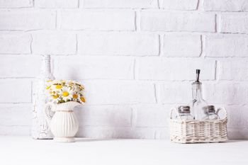 Home interior decoration, bouquet of daisies in white vase, decorative white bottle and glass bottle of oil in a basket. Home interior decoration