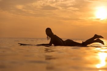 Surfer girl waiting in the line up for a wave at sunrise or sunset