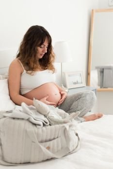 Pregnant woman touching her belly. Happy pregnant woman sitting and touching her belly at home