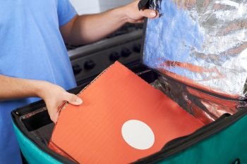 Pizza Delivery Person Putting Food Into Insulated Bag In Restaurant Kitchen