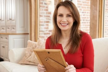 Portrait Of Smiling Mature Woman Looking At Picture Frame At Home
