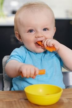 Happy Toddler Sitting At Table Eating Fresh Carrots