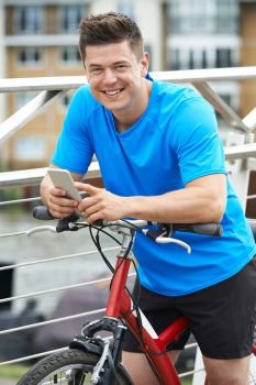 Young Man Using Mobile Phone Whilst Out On Cycle Ride In Urban Setting