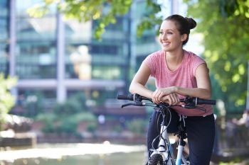 Young Woman Cycling Next To River In Urban Setting
