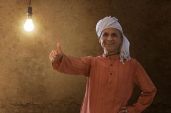 Senior rural man showing thumb up while standing against  light bulb 