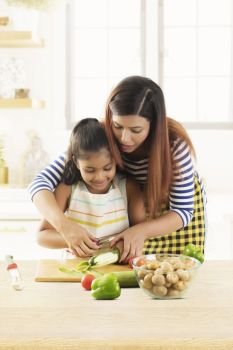 Mother and daughter peeling cucumber in kitchen