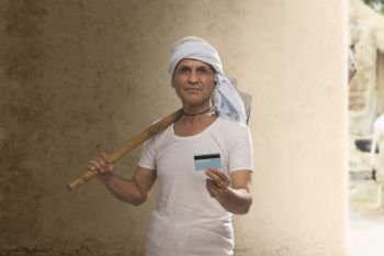 Portrait of Indian old farmer holding credit card and carrying hoe on his shoulder