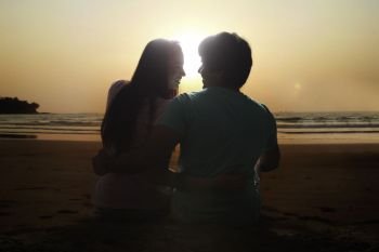 Rear view of young couple sitting together on beach at sunset