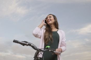 Young woman leaning on bike and talking on phone